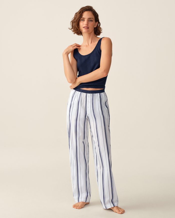 A woman stands barefoot wearing a navy tank top and the Women’s Poplin Romy Pants in Parlor Stripe against a plain light background.