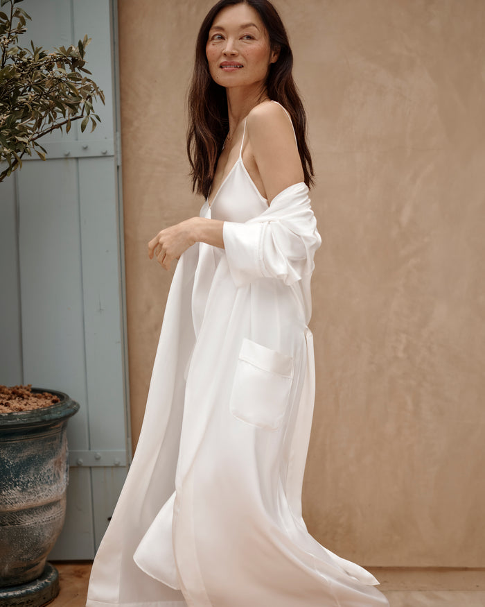 The Petite Plume Womens Silk Long Robe in White boasts a smooth, luxurious fabric with a soft sheen, featuring a wide lapel, long sleeves, and a matching silk waist tie for an elegant and comfortable look.