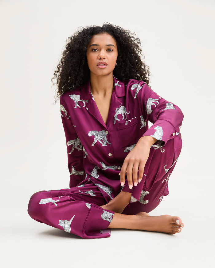 The Women's Silk Pajama Set in Merlot Panthère features a silky, deep magenta button-up shirt and pants adorned with an all-over white illustrated leopard print.