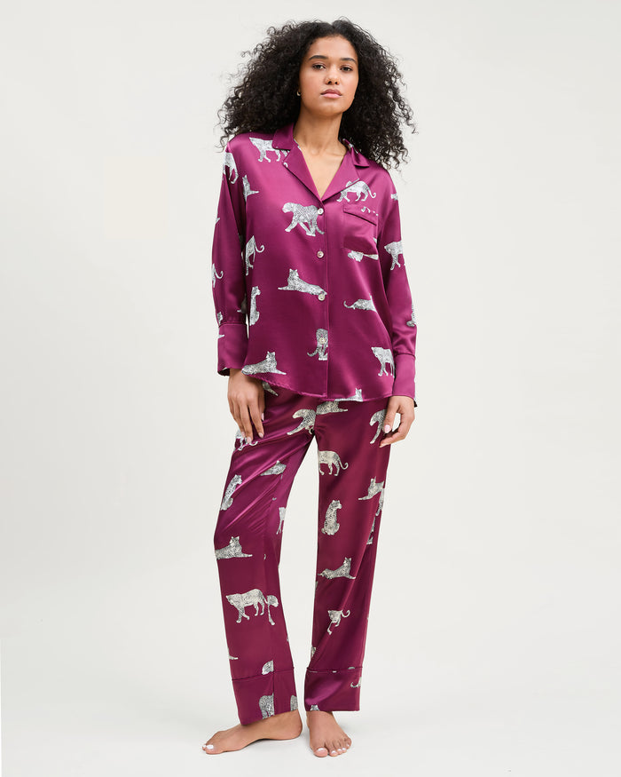 The Women's Silk Pajama Set in Merlot Panthère features a silky, deep magenta button-up shirt and pants adorned with an all-over white illustrated leopard print.