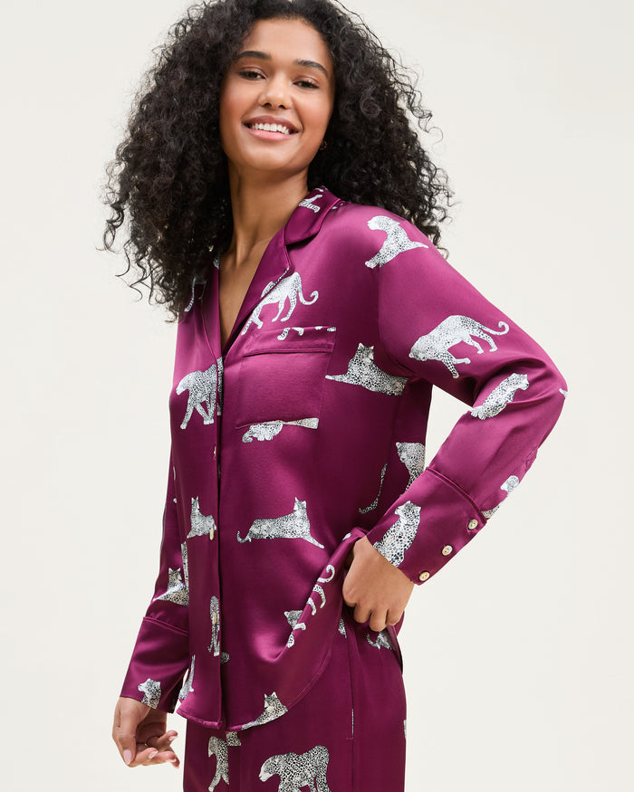 The Women's Silk Pajama Set in Merlot Panthère features a silky, deep magenta button-up shirt and pants adorned with an all-over white illustrated leopard print.