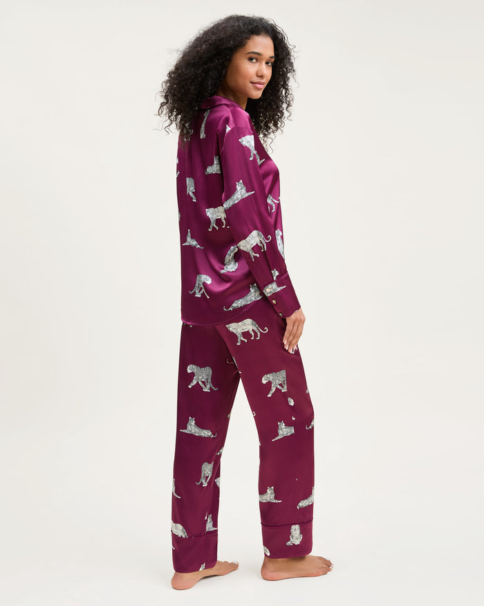 The Women's Silk Pajama Set in Merlot Panthère features a silky, deep magenta button-up shirt and pants adorned with an all-over white illustrated leopard print.