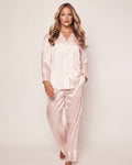 A person with long, wavy blonde hair wears Petite Plumes Womens Silk Pajama Set in Pink Stripe as they walk towards the camera on a light background, highlighting the timeless elegance of their luxury sleepwear.