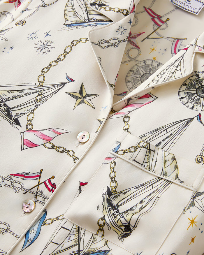 Close-up of the Women’s Silk Pajama Set in Regatta Royale, showcasing a cream-colored fabric adorned with a nautical pattern of sailboats, ropes, stars, compasses, and flags. Features include iridescent buttons and a visible chest pocket.