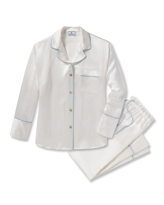 The Petite Plume Womens Silk Pajama Set, in white with periwinkle piping, includes a silky top with long sleeves, buttons, a notched collar, and chest pocket. The pants have an elastic waistband. Ideal as a bridal keepsake, they are elegantly arranged on a solid white background.