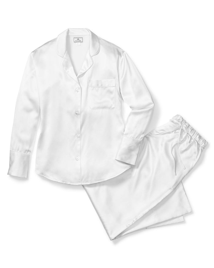 The Womens Silk Pajama Set in White by Petite Plume includes luxury sleepwear with a long-sleeve button-up shirt and chest pocket, paired with matching pants featuring an elastic waistband. The 22mm silk fabric is smooth and shiny.