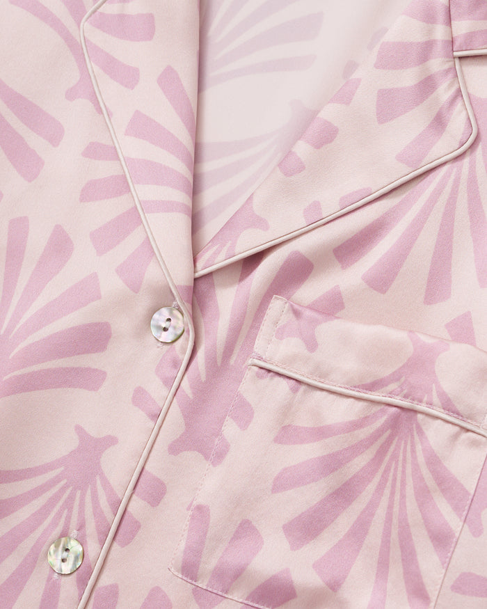 The Women's Silk Short Sleeve Short Set in Blush Tide features a matching pink button-up top and elastic-waist shorts, both adorned with a light purple geometric fan pattern.