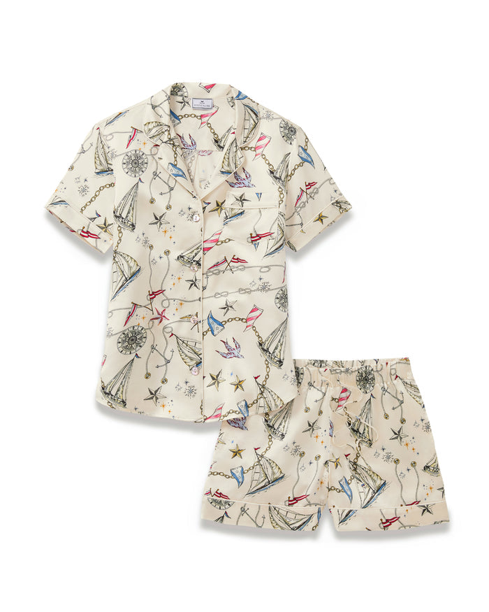 Women’s Silk Short Sleeve Short Set in Regatta Royale, featuring a cream-colored short-sleeve button-up shirt and matching shorts with a nautical-themed print showcasing boats, compasses, stars, and chains in shades of blue, red, black, and gold.