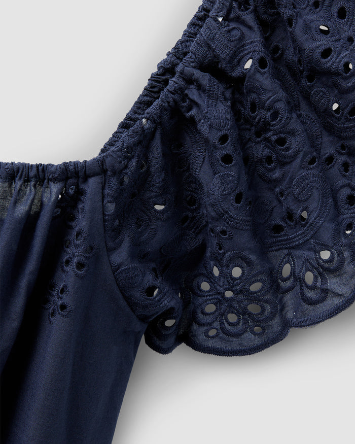 Close-up of a Womens Twill Ava Nightgown in Navy by Petite Plume, showcasing dark blue fabric with intricate lace embroidery and eyelet details. Crafted from premium cotton, it features ruffled edges and an elastic band against a solid light gray background.