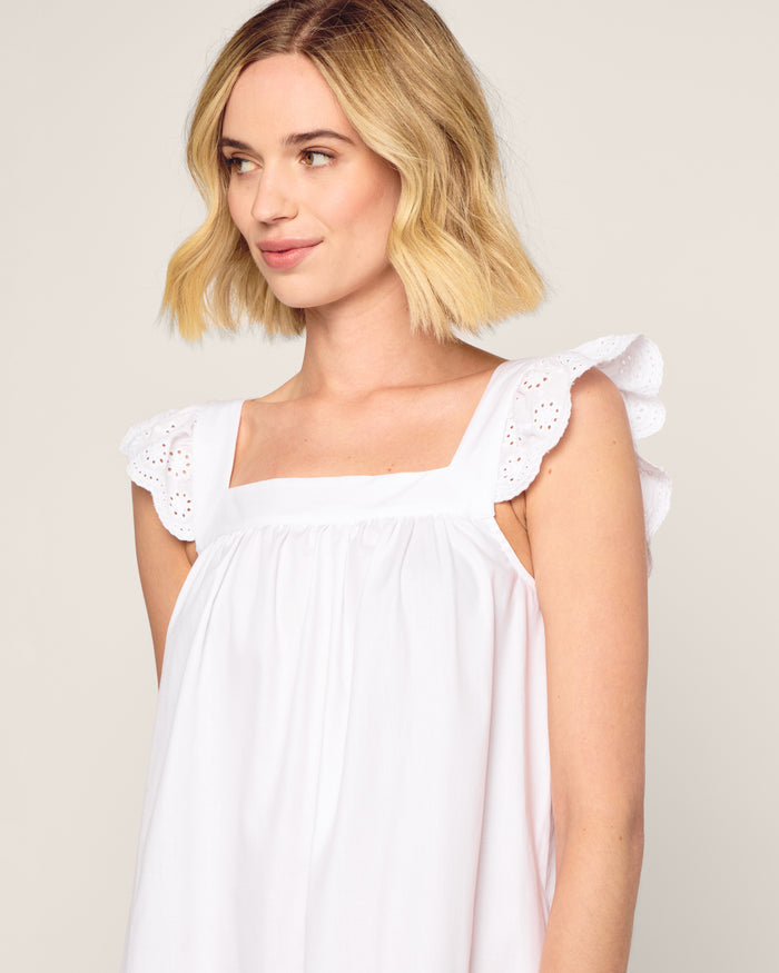 A woman with shoulder-length blonde hair wearing a luxurious Petite Plume Womens Twill Clara Nightgown in White, detailed with elegant eyelet lace ruffles and crafted from high-quality cotton, gazes to the side against a neutral background.
