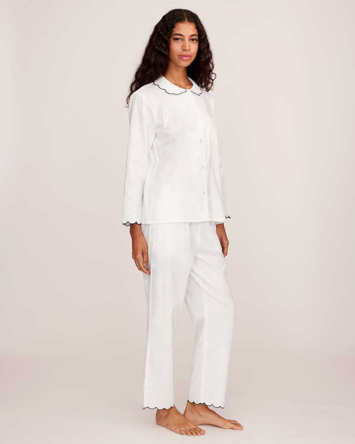 A person stands barefoot wearing the Women’s Twill Colette Pajama Set in White with Navy Piping, posing against a plain light background.