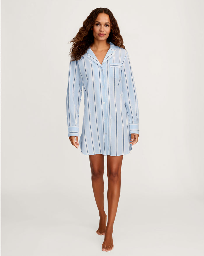 A woman with wavy brown hair stands barefoot against a plain white background, wearing the Women’s Twill Nightshirt in Coastal Stripe.
