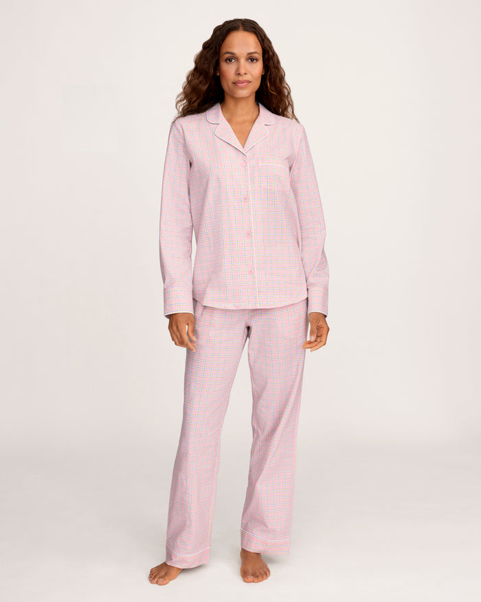 A woman with long curly hair wears the Women's Twill Pajama Set in Peony Plaid, standing barefoot against a plain light background and facing the camera with a relaxed expression.