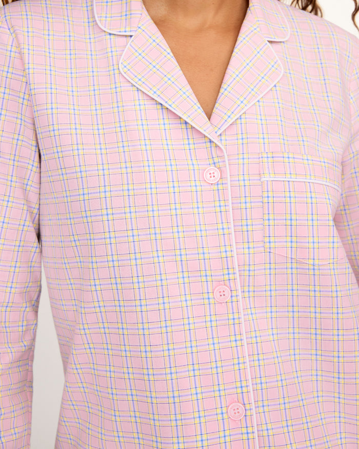 A woman with long curly hair wears the Women's Twill Pajama Set in Peony Plaid, standing barefoot against a plain light background and facing the camera with a relaxed expression.