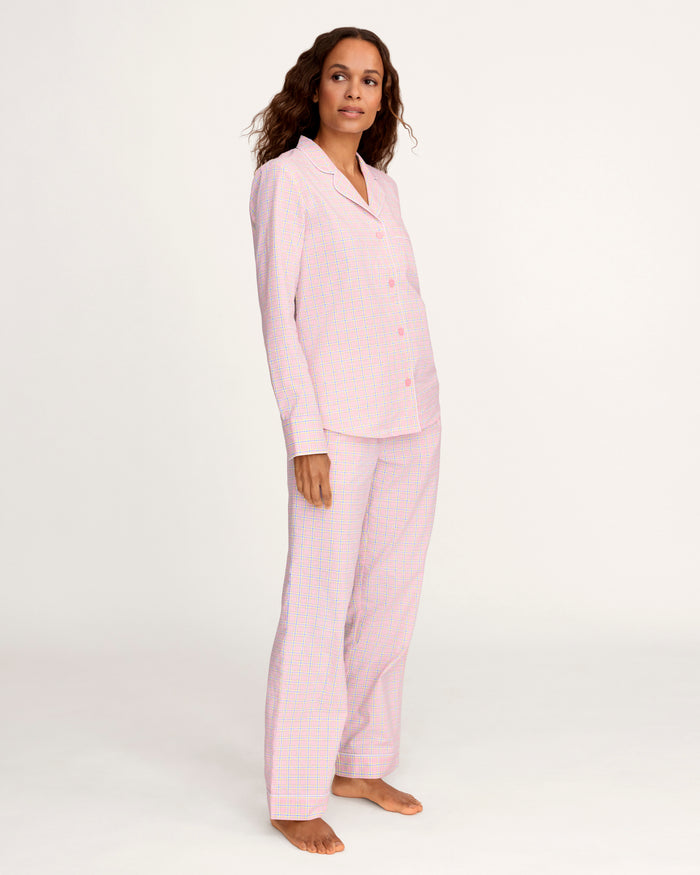 A woman with long curly hair wears the Women's Twill Pajama Set in Peony Plaid, standing barefoot against a plain light background and facing the camera with a relaxed expression.