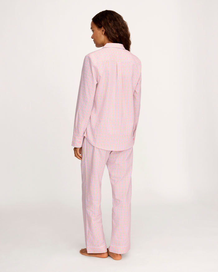 A woman with long curly hair wears the Women's Twill Pajama Set in Peony Plaid, standing barefoot against a plain light background and facing the camera with a relaxed expression.
