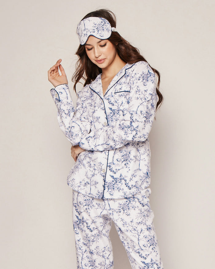A woman models the Women’s Twill Pajama Set in Timeless Toile with a coordinating sleep mask, standing against a plain background. She gently touches her hair with one hand while crossing the other arm, gazing down with a relaxed expression.