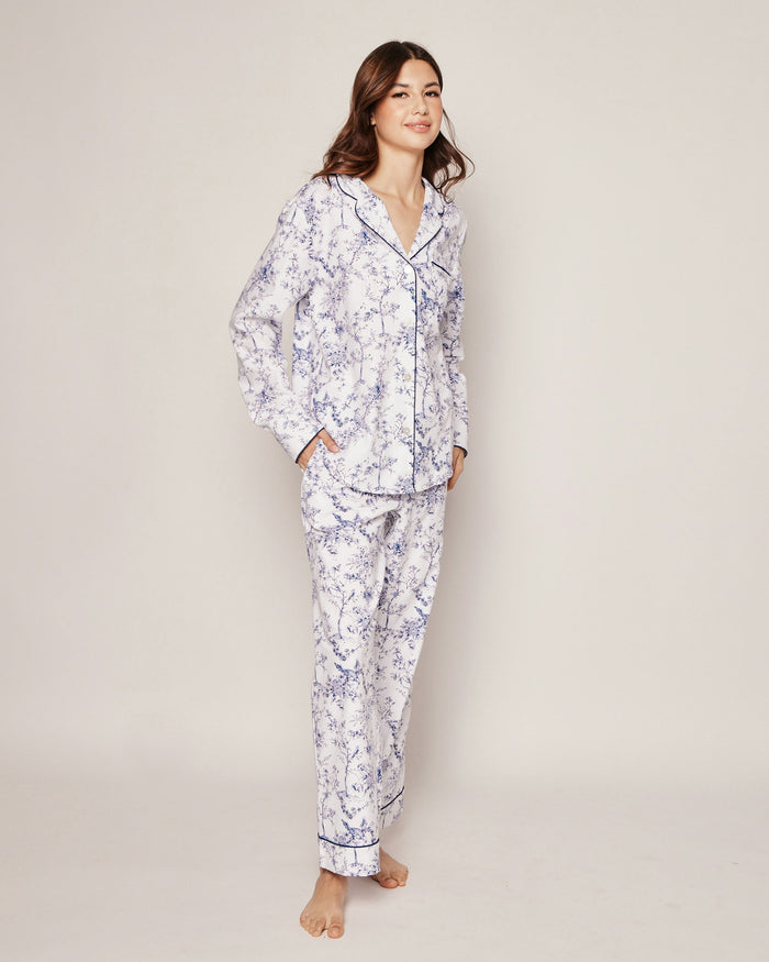 A woman stands barefoot, smiling, wearing the Women’s Twill Pajama Set in Timeless Toile—a matching long-sleeve set featuring a white and blue floral pattern—against a plain light background.
