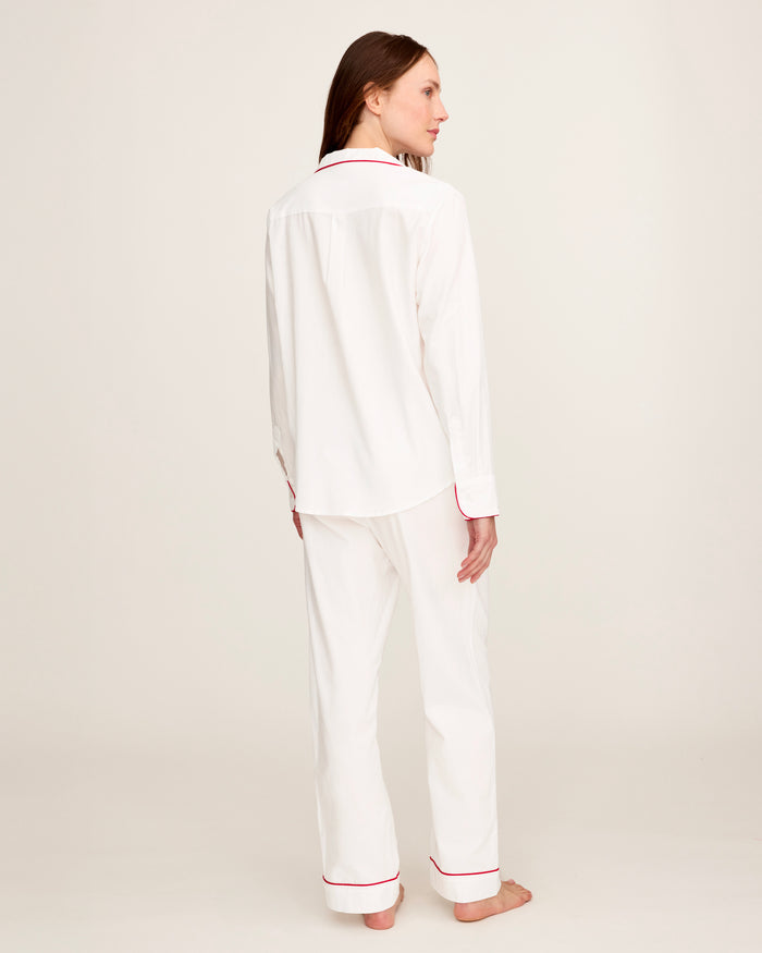 A woman stands barefoot in the Women's Twill Pajama Set in White with Red Piping against a plain, light background.