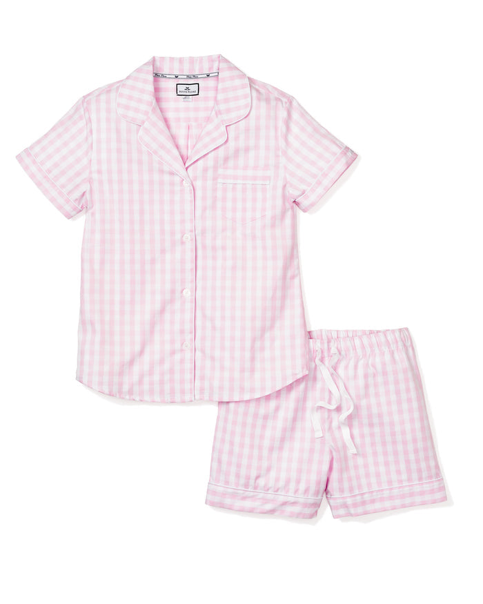 The Womens Twill Pajama Short Set in Pink Gingham by Petite Plume is a luxurious two-piece set with a soft cotton top featuring buttons and a chest pocket, paired with shorts that have an elastic waistband and white drawstring for comfort.