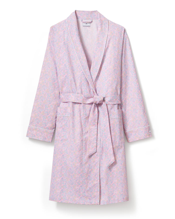 A woman stands barefoot against a plain light background, wearing the Women's Twill Robe in Fleur Blush—a knee-length, long-sleeved, light pink robe with a subtle floral pattern and waist tie.
