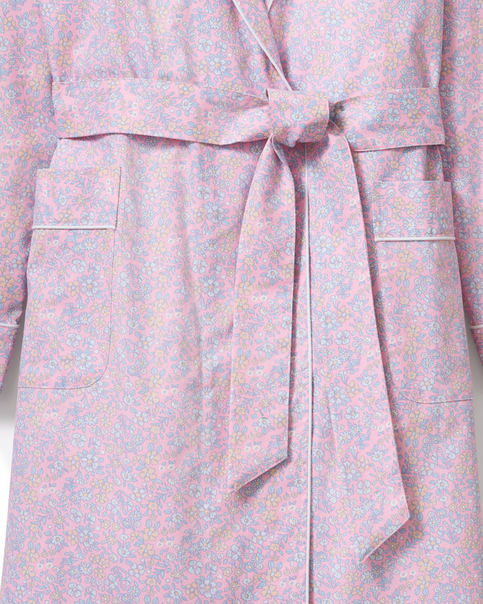 A woman stands barefoot against a plain light background, wearing the Women's Twill Robe in Fleur Blush—a knee-length, long-sleeved, light pink robe with a subtle floral pattern and waist tie.