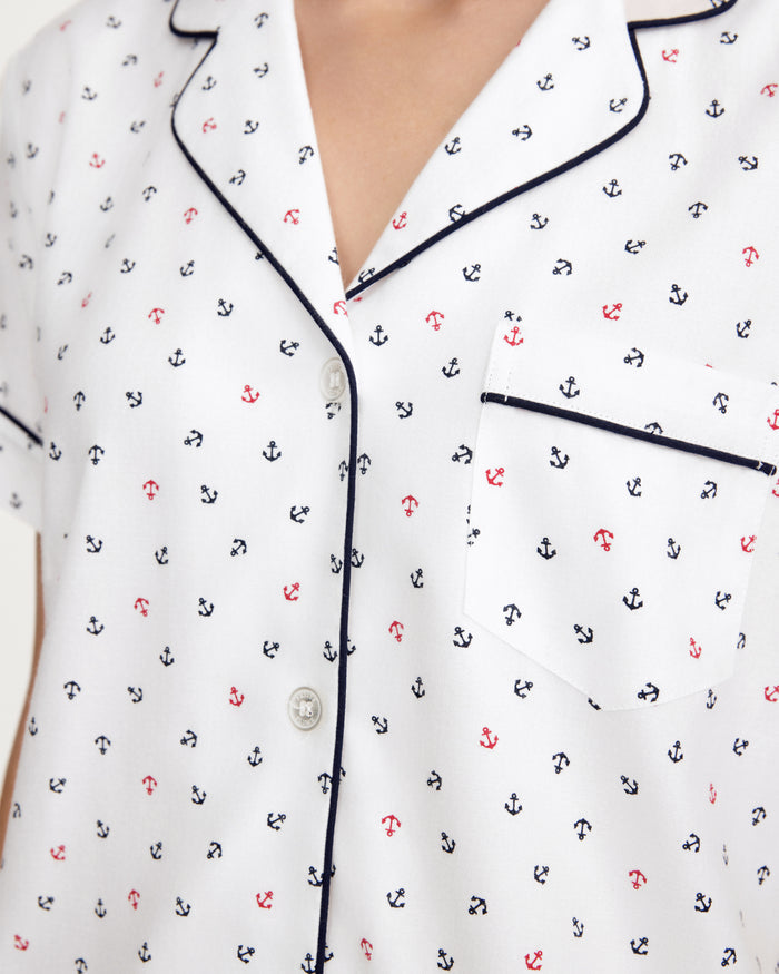 A close-up of the Women’s Twill Short Sleeve Short Set in Anchors Away White, featuring a white pajama top with a navy blue and red anchor pattern, black piping along the edges, white buttons, and a chest pocket.
