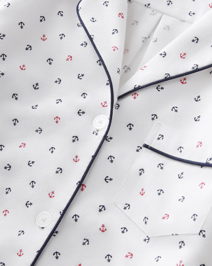Women’s Twill Short Sleeve Short Set in Anchors Away White: A white pajama shirt featuring small blue and red anchor patterns, navy blue piping along the edges, a front pocket, and white buttons.