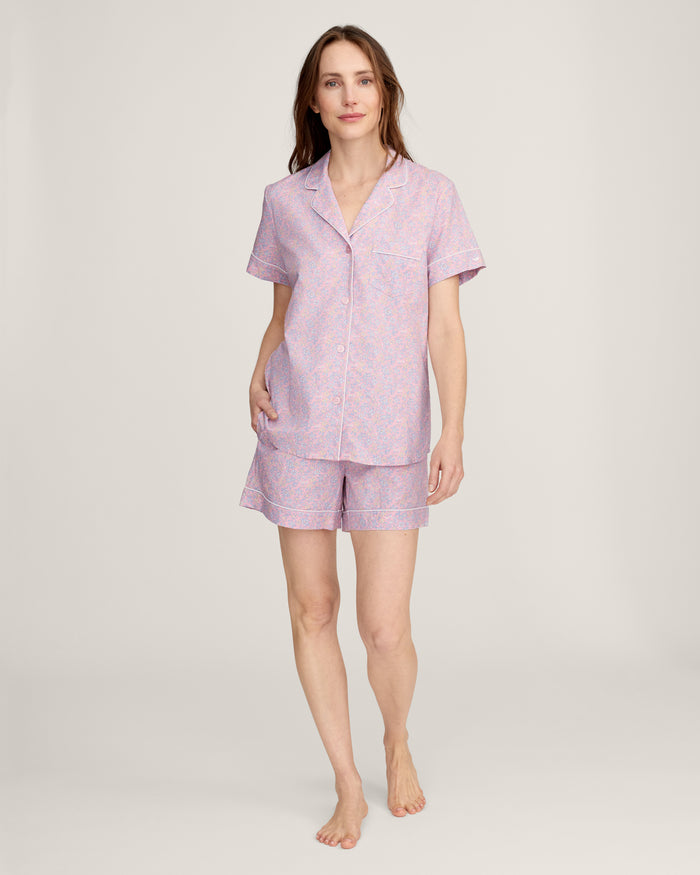 A woman with long brown hair is wearing the Women's Twill Short Sleeve Short Set in Fleur Blush and smiling softly, standing in front of a plain light background.