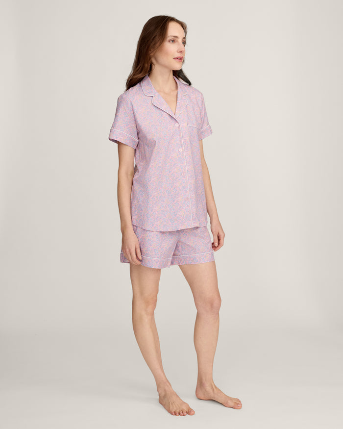 A woman with long brown hair is wearing the Women's Twill Short Sleeve Short Set in Fleur Blush and smiling softly, standing in front of a plain light background.