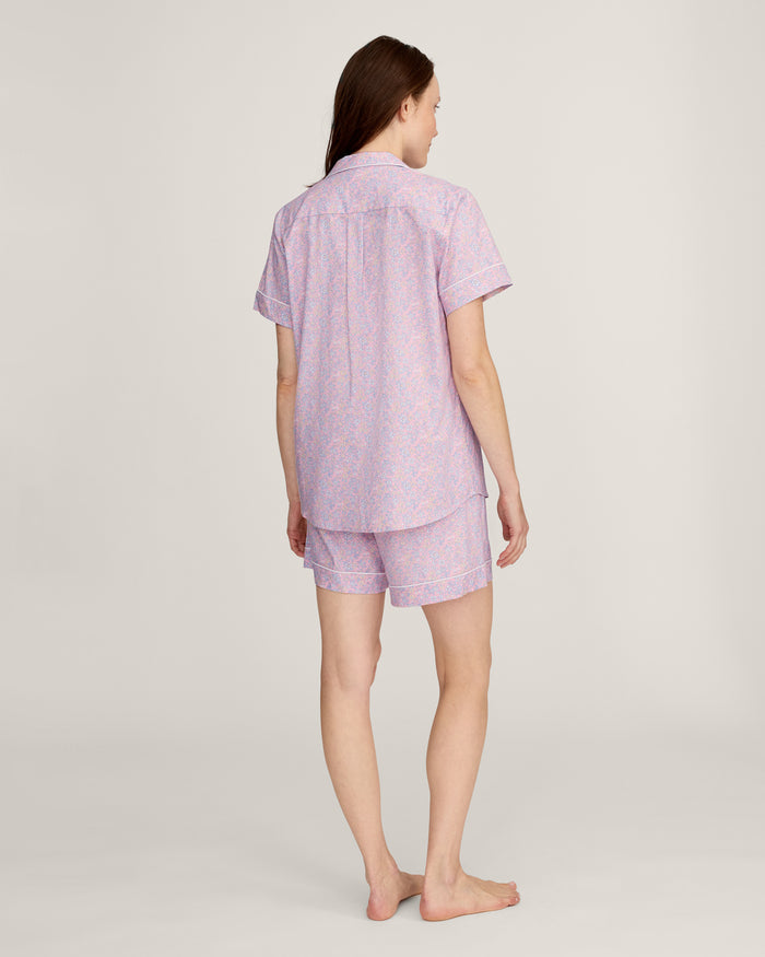 A woman with long brown hair is wearing the Women's Twill Short Sleeve Short Set in Fleur Blush and smiling softly, standing in front of a plain light background.