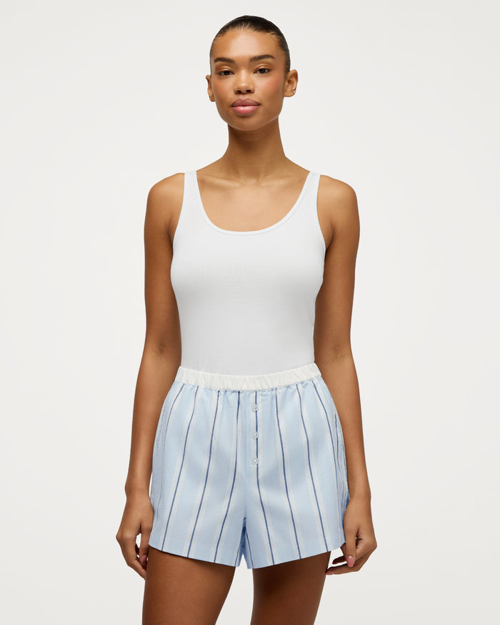 A woman wearing the Women’s Twill Sleep Short in Coastal Stripe and a white tank top stands against a plain white background, facing forward with a neutral expression.