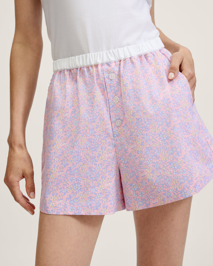 A woman wearing a white sleeveless tank top and Women's Twill Sleep Shorts in Fleur Blush stands with one hand in her pocket against a plain light background.