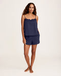 A woman stands barefoot against a plain background, wearing the Women's Voile Fleur Cami Short Set in Navy. She has wavy hair and her hands are in her pockets.