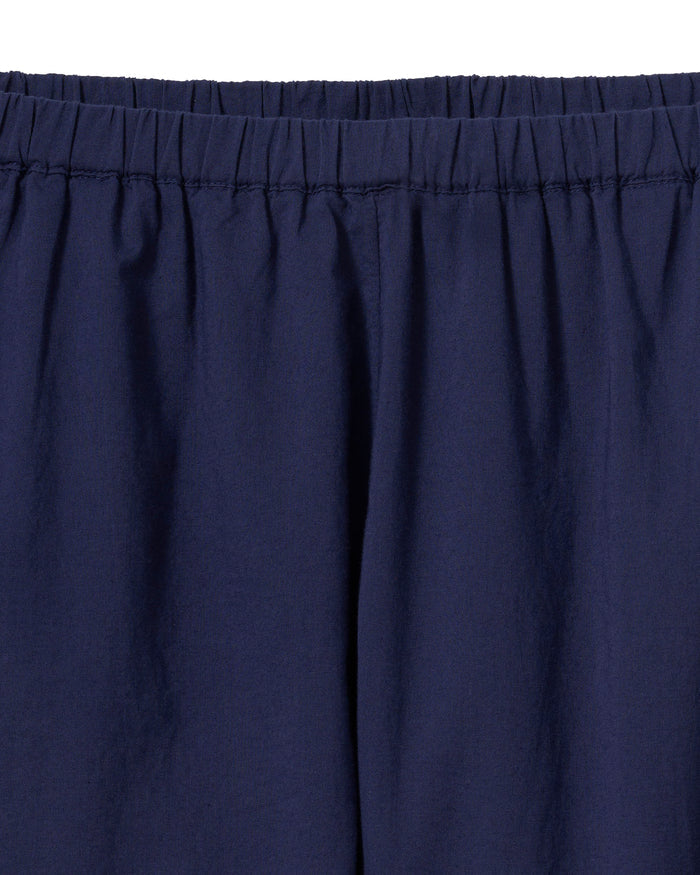 A woman stands barefoot against a plain background, wearing the Women's Voile Fleur Cami Short Set in Navy. She has wavy hair and her hands are in her pockets.